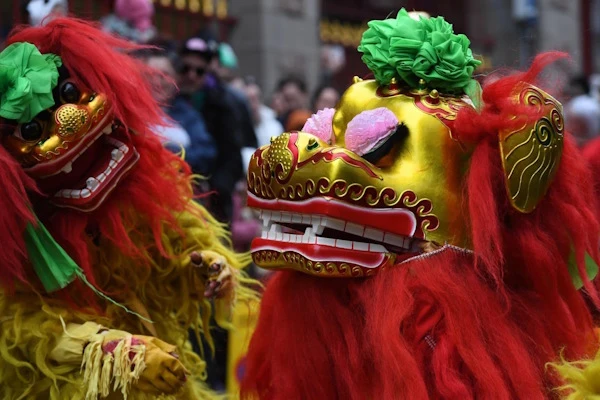 Close-up image of the head of an adult Chinese Lion and a baby Lion during a street performance.