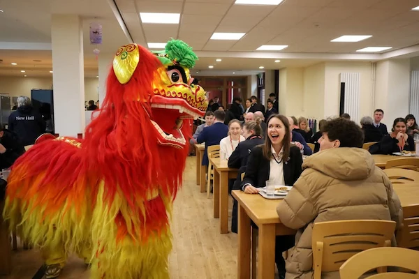 A Chinese Lion entertains two guests who are eating at a table; the lady has a surprised and happy expression