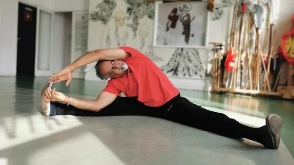 Student performs box splits and is leaning to one side both hands on his foot