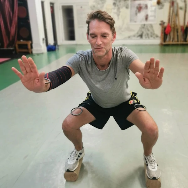 Student performs Ma Bu or horseriding stance, on raised planks and while balancing rings on his arms and legs