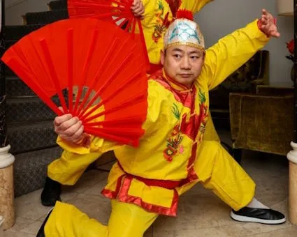image of Shifu dressed in yellow costume in a pose holding an open fan