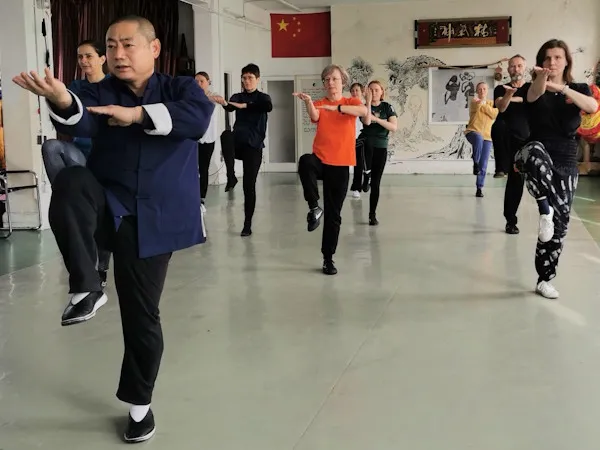 Shifu teaching a Tai Chi class balancing on one leg while students follow