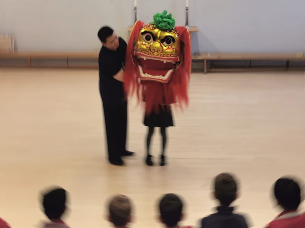 A school student tries on the lion dance costume head, helped by an instructor